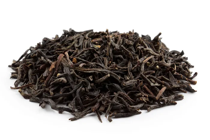 Mound of dark twisted loose-leaf Assam black tea with golden tips on a white background