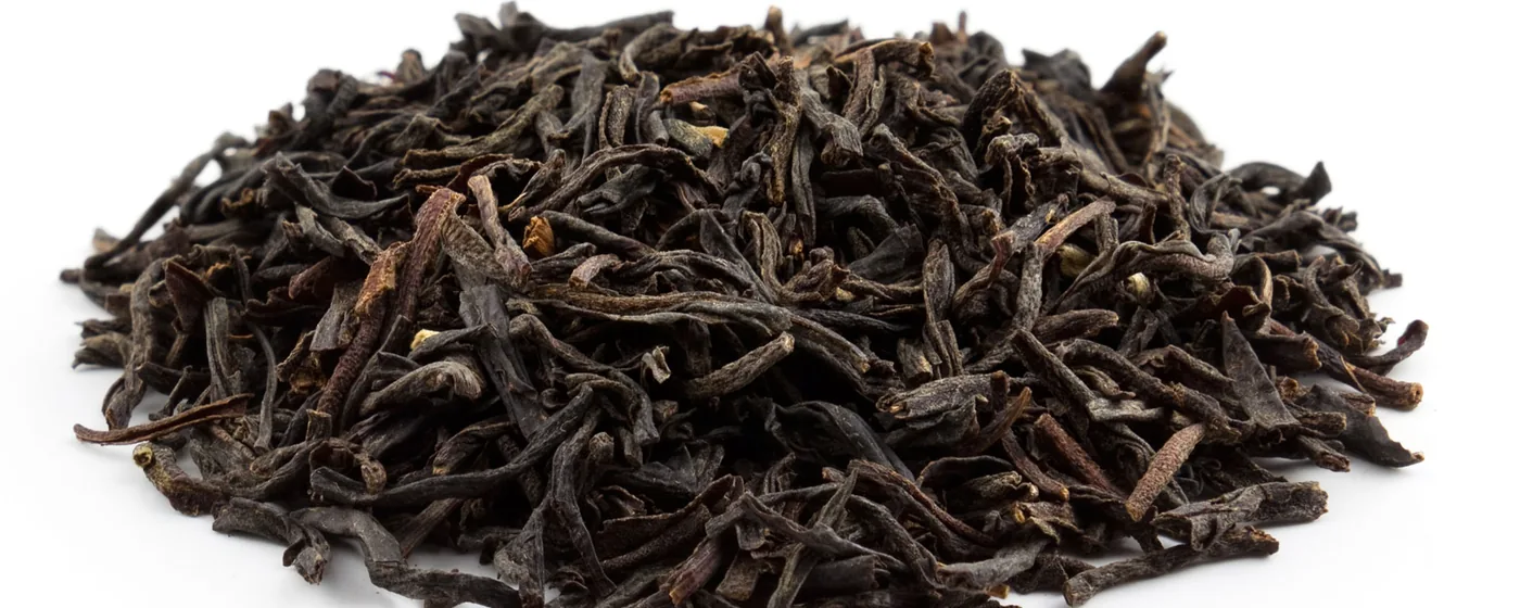 Mound of dark twisted loose-leaf Assam black tea with golden tips on a white background