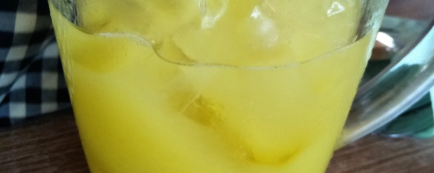 Glass of golden turmeric drink over ice with a straw on a wooden table