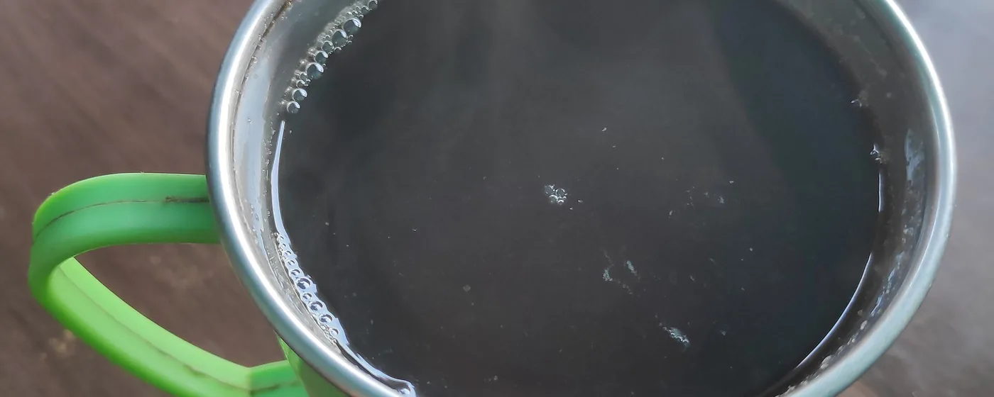 Green mug of dark ginger tea on a wooden table, viewed from above