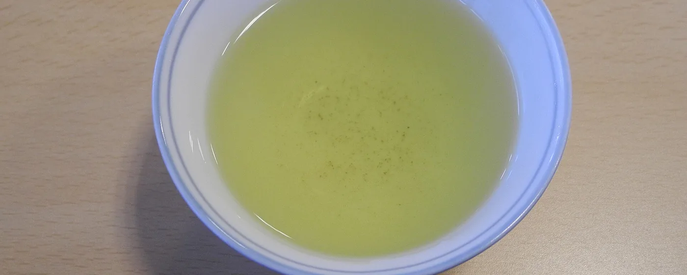 Overhead view of pale green tea in a white blue-rimmed bowl on a light wooden table