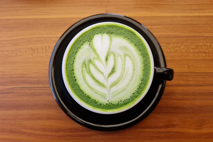Overhead view of a bright green matcha latte with white rosetta latte art in a black cup on wood