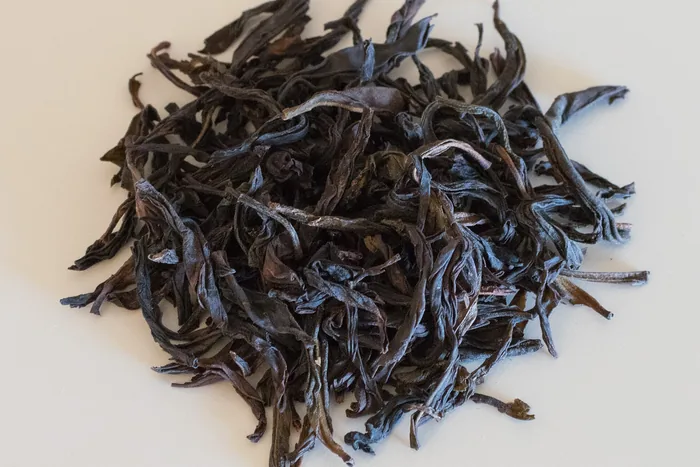 Pile of long, dark, twisted dry oolong tea leaves on a pale cream background