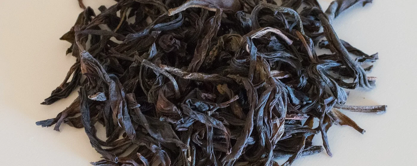 Pile of long, dark, twisted dry oolong tea leaves on a pale cream background