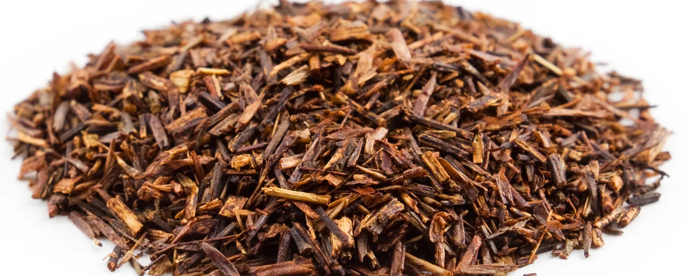 Heap of dried cut rooibos tea, reddish-brown needle-like leaf pieces, on a white background