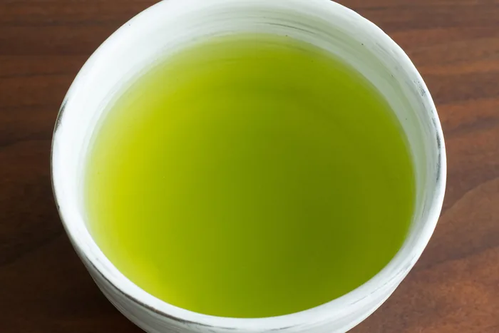 Vivid green sencha tea in a white ceramic cup on a dark wooden table, viewed from above