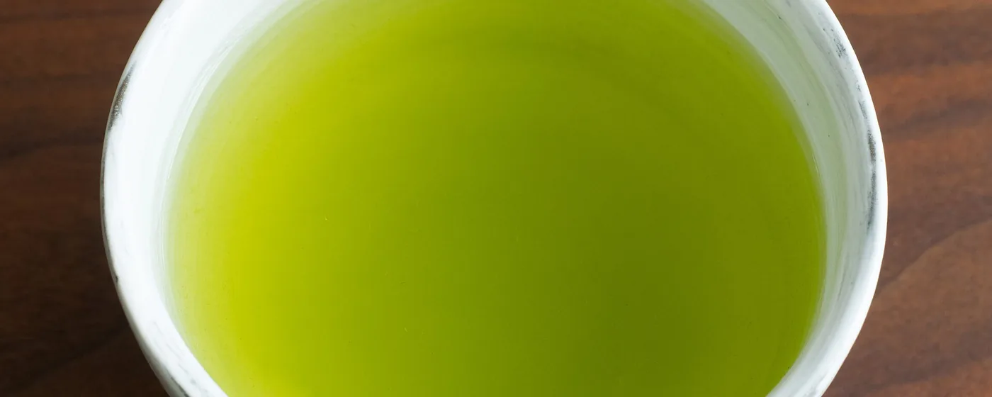 Vivid green sencha tea in a white ceramic cup on a dark wooden table, viewed from above