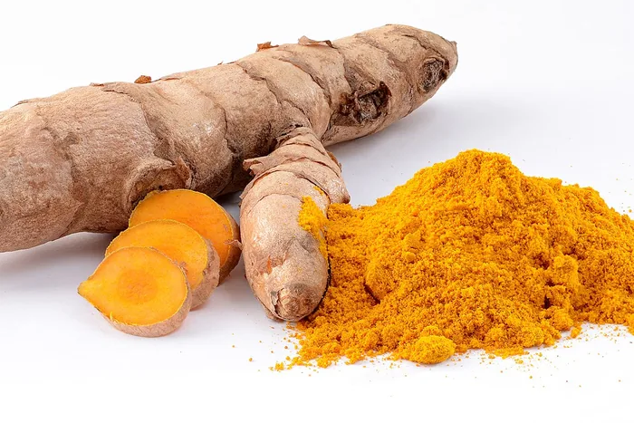 Whole turmeric rhizome with bright orange cut slices beside a mound of golden turmeric powder