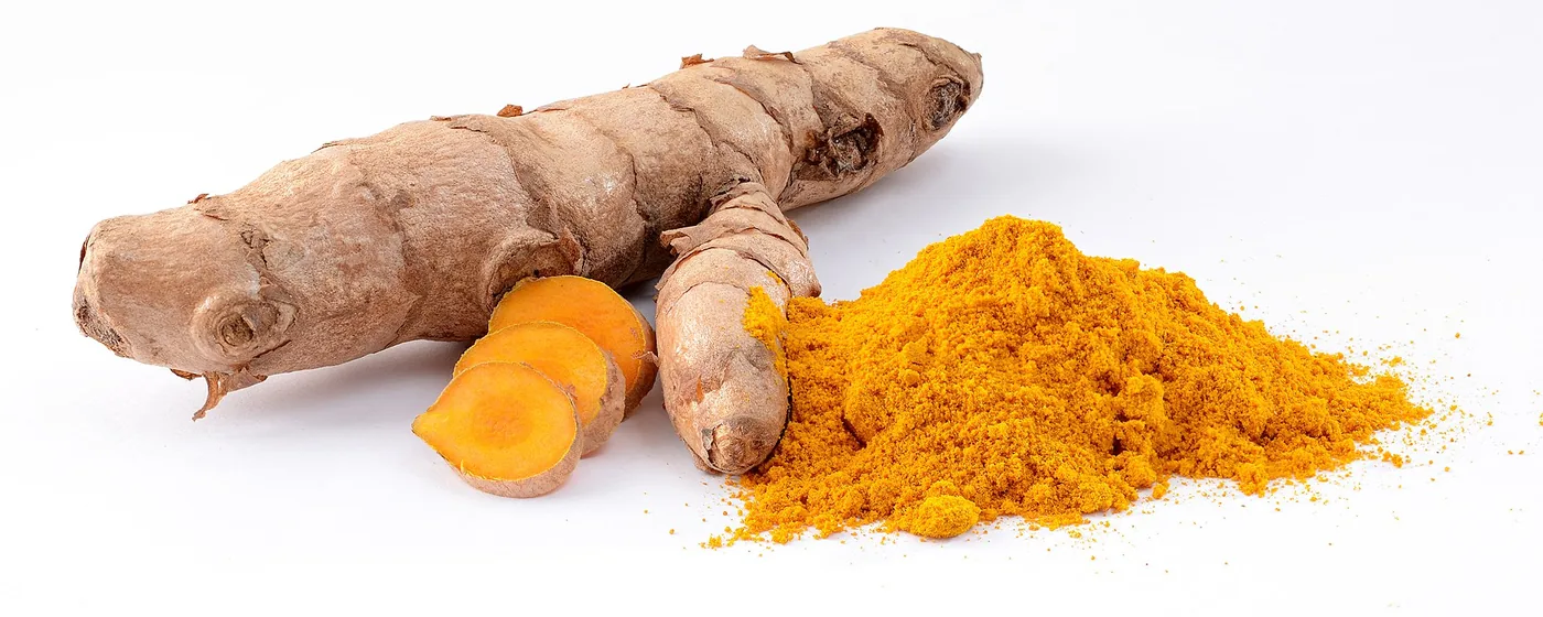 Whole turmeric rhizome with bright orange cut slices beside a mound of golden turmeric powder